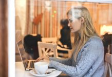 7 Ways To Organize Your OnlyFans Feed Like A Pro Blonde woman in a blue sweater using a laptop in a cozy café setting.