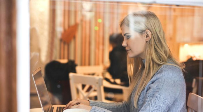 7 Ways To Organize Your OnlyFans Feed Like A Pro Blonde woman in a blue sweater using a laptop in a cozy café setting.