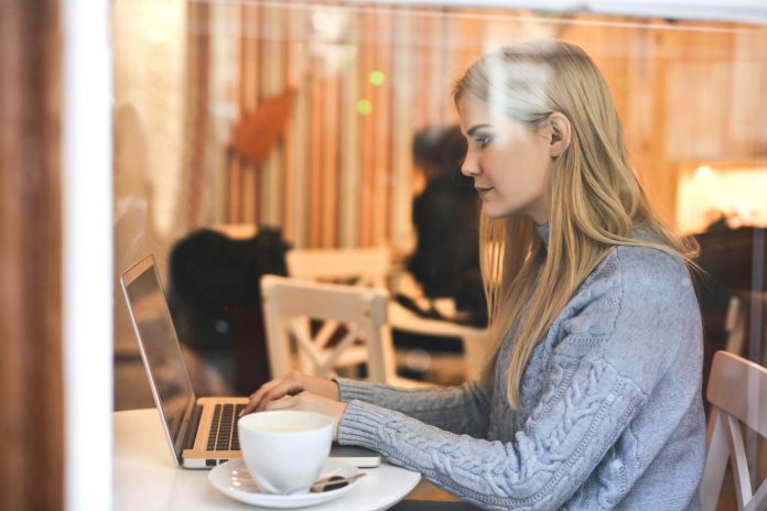 Photo by Andrea Piacquadio Blonde woman in a blue sweater using a laptop in a cozy café setting.